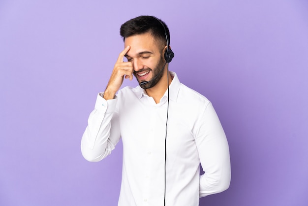 Telemarketer man working with a headset isolated on purple background laughing