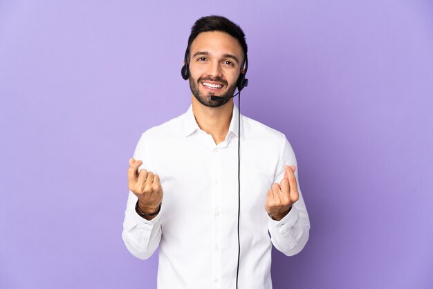 Telemarketer man working with a headset isolated on purple background making money gesture