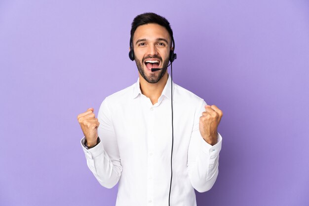 Uomo di telemarketer che lavora con una cuffia avricolare isolata sulla parete viola che celebra una vittoria nella posizione del vincitore