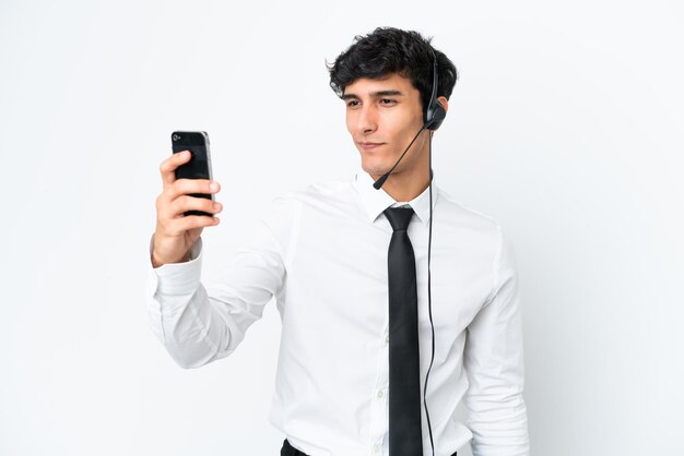 Telemarketer man working with a headset isolated on white background making a selfie