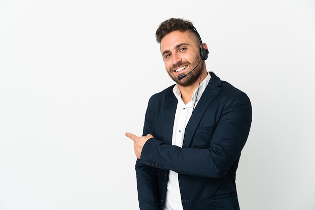 Telemarketer man working with a headset isolated on white background pointing back