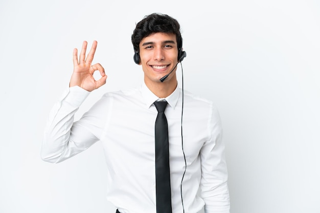 Telemarketer man working with a headset isolated on white background showing ok sign with fingers