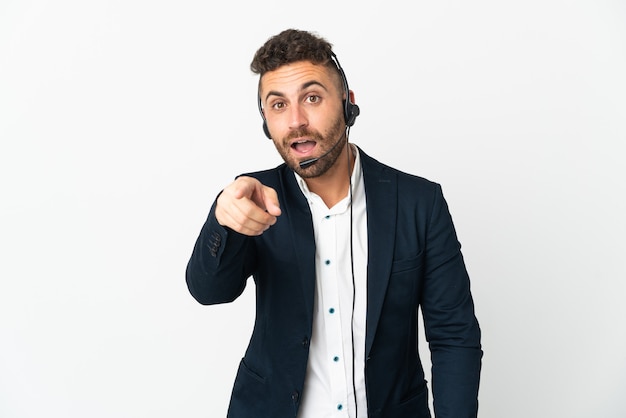 Telemarketer man working with a headset isolated on white background surprised and pointing front