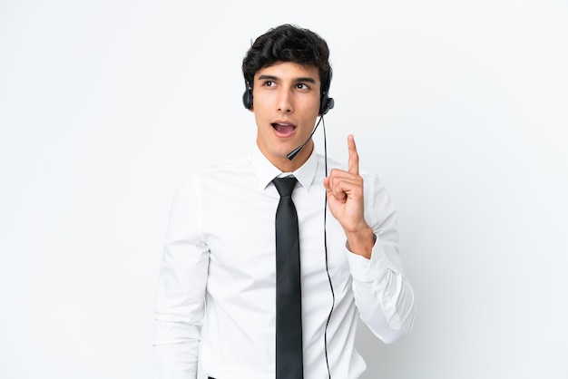 Telemarketer man working with a headset isolated on white background thinking an idea pointing the finger up