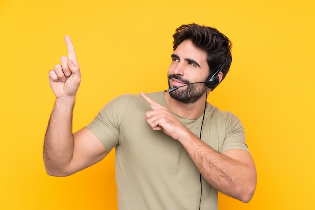 Telemarketer man working with a headset over isolated yellow wall pointing with the index finger a great idea