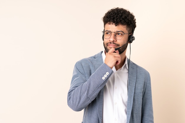 Telemarketer Moroccan man working with a headset isolated on beige wall and looking up