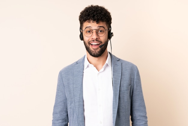 Telemarketer Moroccan man working with a headset isolated on beige wall with surprise facial expression