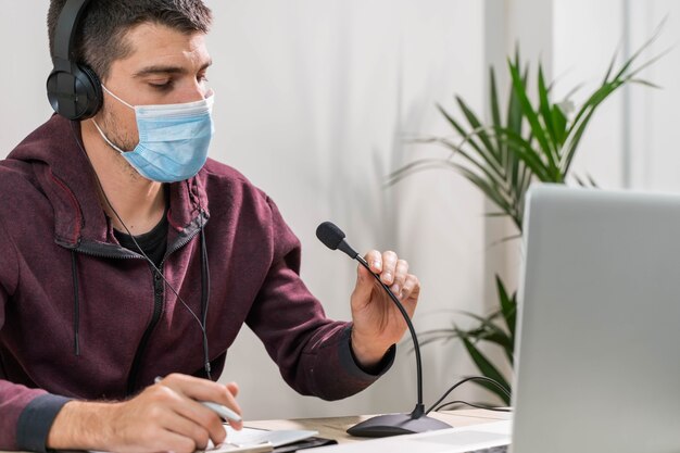 Telemarketer or podcast man working with laptop and talking on a headset with face mask at office