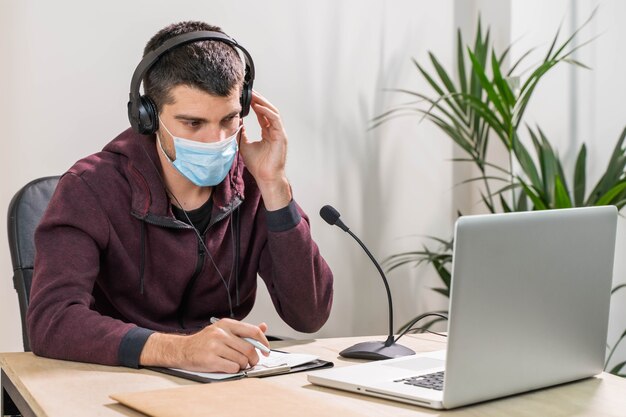 Telemarketer or podcast man working with laptop and talking on a headset with face mask at office