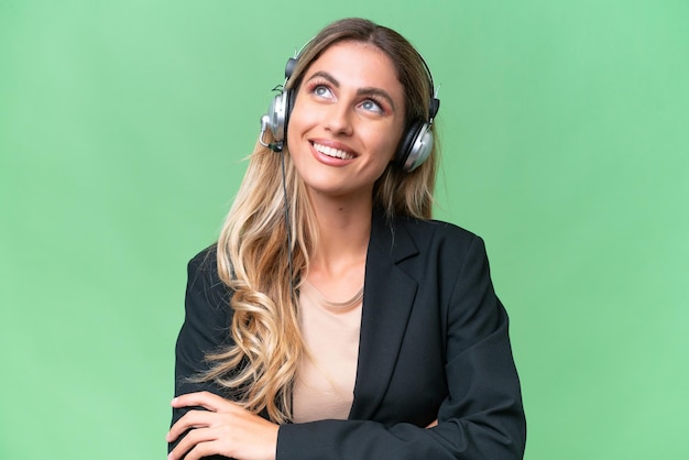 Telemarketer pretty Uruguayan woman working with a headset over isolated background looking up while smiling