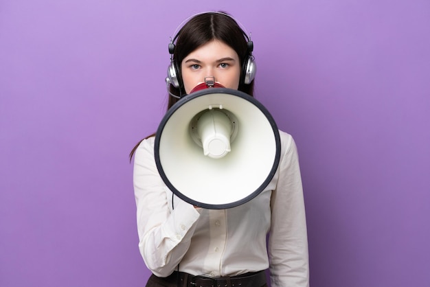 Telemarketer Russian woman working with a headset isolated on purple background shouting through a megaphone