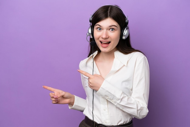 Telemarketer Russian woman working with a headset isolated on purple background surprised and pointing side
