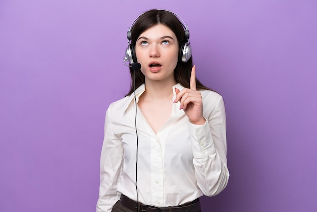 Telemarketer Russian woman working with a headset isolated on purple background thinking an idea pointing the finger up