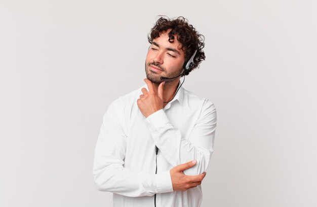 Telemarketer smiling with a happy, confident expression with hand on chin, wondering and looking to the side