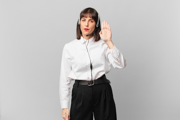 Telemarketer woman looking serious, stern, displeased and angry showing open palm making stop gesture