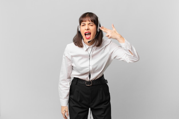 Telemarketer woman looking unhappy and stressed, suicide gesture making gun sign with hand, pointing to head