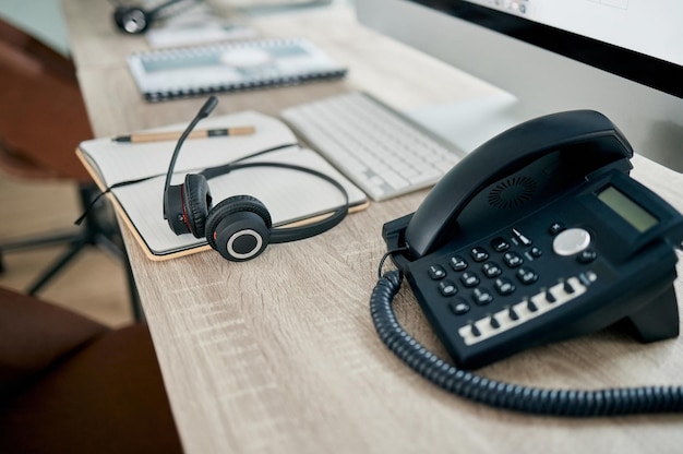 Telemarketing kantoortelefoon en VOIP op bureau voor communicatie, neem contact met ons op en advies via computer Moderne kantoortelefoon en koptelefoon op tafel voor klantenondersteuning, hulp of service met pc