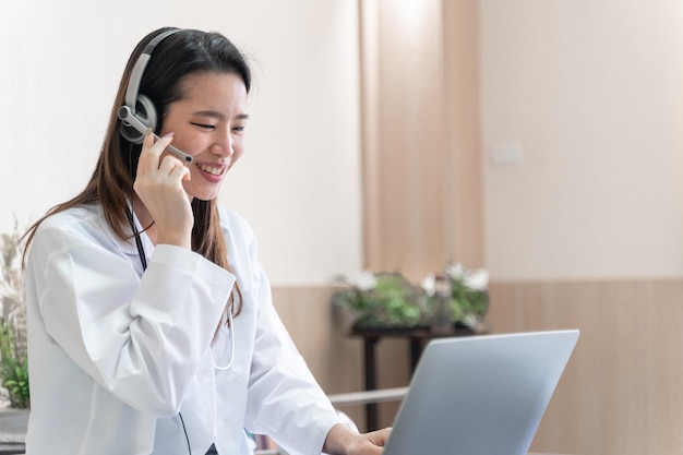 Telemedicine concept Asian woman doctor in headset taking calling on her headset microphone online for a ache patient