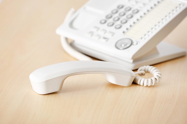 Telephone with picked up receiver on wooden table in office