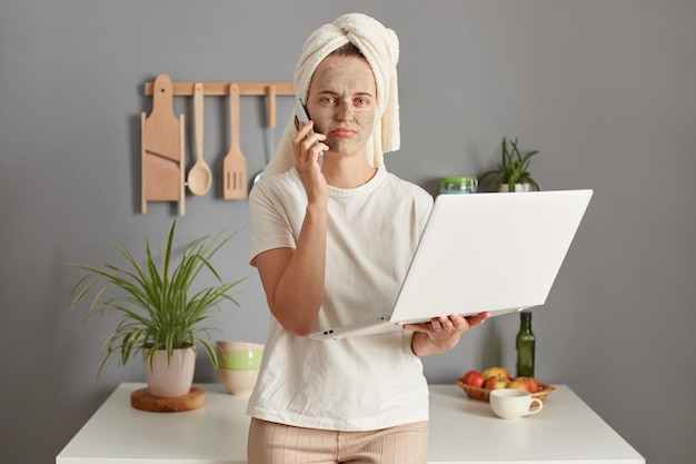 Teleurgesteld ontevreden jonge vrouw poseren in de keuken met handdoek op het hoofd online werken met problemen op het werk met een notitieboekje pratende telefoon met droevige uitdrukking