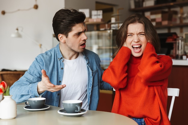 Teleurgesteld paar vrouw en man 20s schreeuwen en hebben ruzie, terwijl ze koffiepauze hebben in café