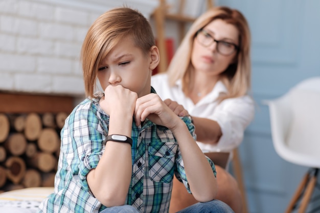 Teleurgestelde jongen die een geruit overhemd draagt en zijn handen in vuisten houdt terwijl hij naar beneden kijkt