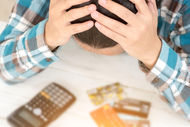 Foto teleurgestelde man met het hoofd in de handen terwijl hij aan tafel zit met creditcards