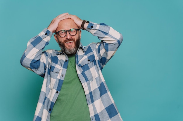 Teleurgestelde medio volwassen blanke bebaarde man in geruit casual shirt en bril houdt hoofd gefrustreerd kijkt naar camera met verstoorde gezichtsuitdrukking tegen turquoise studio achtergrond Mockup