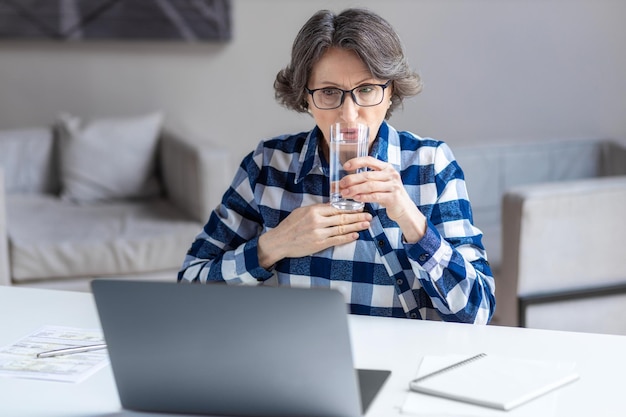 Teleurgestelde oude vrouw die aan tafel zit, voelt zich gefrustreerd door onverwacht slecht nieuws op laptop van bank- of cyberpestenconcept