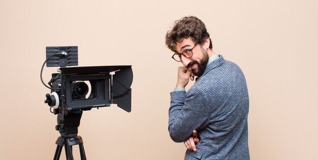 Foto televisiepresentator die met een gelukkige, zekere uitdrukking met hand op kin glimlacht, zich benieuwd en aan de kant kijkt