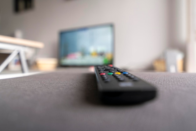 Television control on sofa with defocused television in\
background