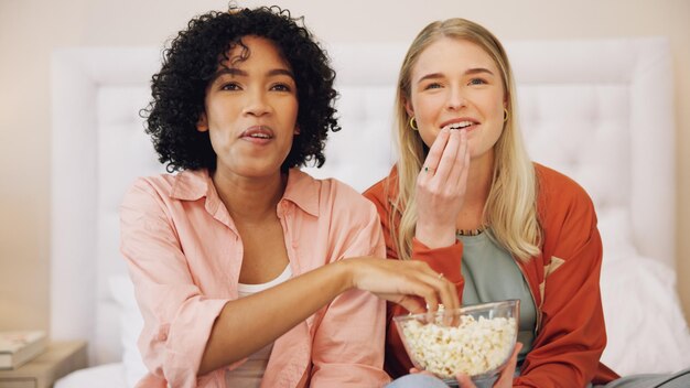 Television happy and women friends on a bed with popcorn for movie comedy or standup show at home Comic snack and ladies watching tv in a bedroom laugh bond and relax with streaming subscription
