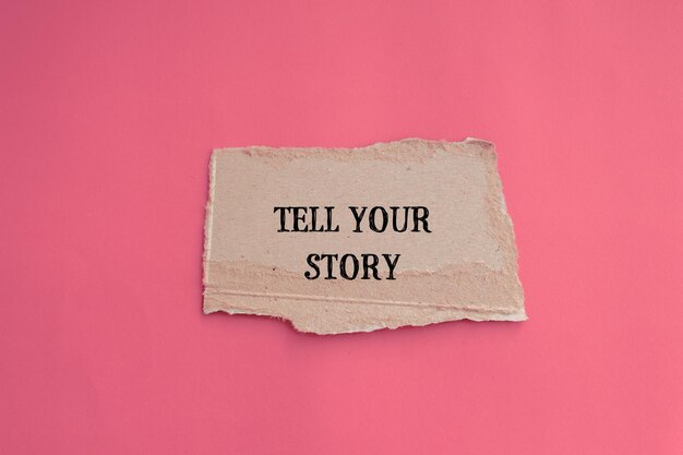 Tell your story lettering on ripped paper piece with pink background Conceptual photo Top view