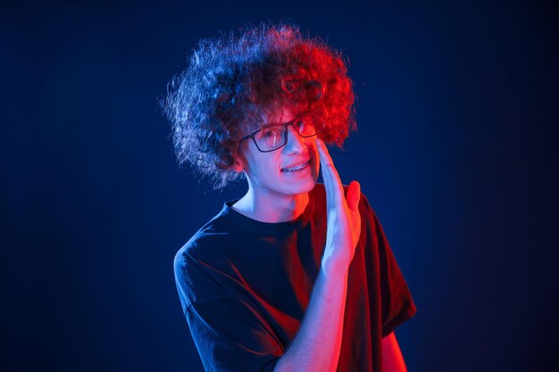 Telling a secret young man with curly hair is indoors illuminated by neon lighting