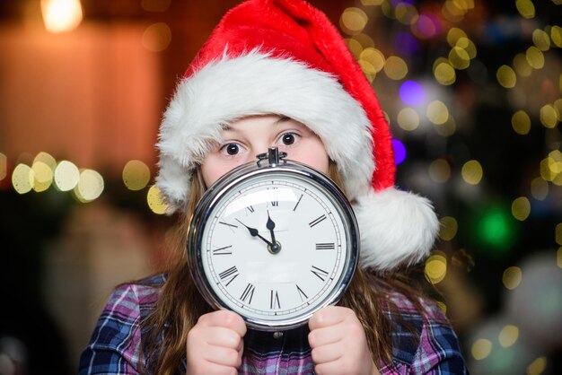 Telt tijd Een paar minuten tot het nieuwe jaar Magisch moment komt Kerstmis bijna hier Meisje kerstman hoed en klok Ontmoet kerst vakantie feestelijke sfeer kerstdag Nieuwjaar aftellen