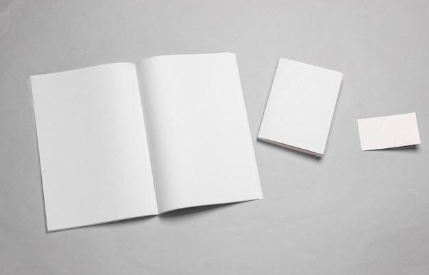 Template for design Mockup of an open magazine or notebook with white pages a book with an empty cover and a business card on a gray background Flat lay