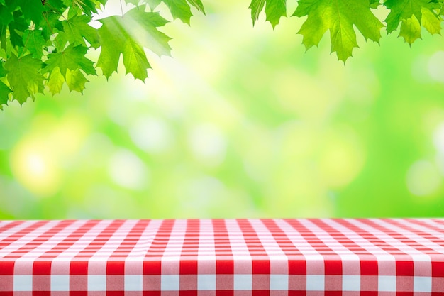 Template for outdoor cooking fresh green maple leaves over an empty table with classic Italian red checkered tablecloth on a sunny day with copy space