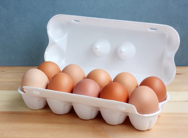 Ten chicken brown eggs in a white Styrofoam package on the wooden table.