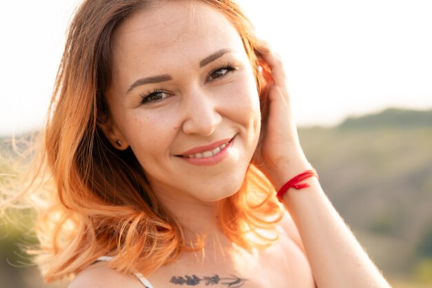 Tender beautiful red-haired girl enjoys the sunset in a field with a hill