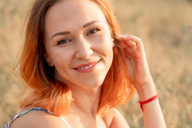 Tender beautiful red-haired girl enjoys the sunset in a field with a hill.