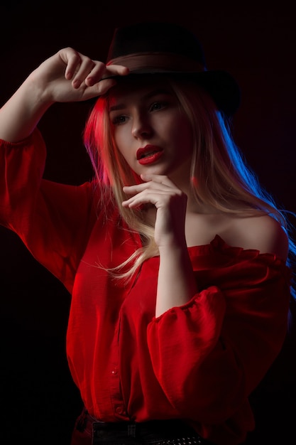 Tender blonde woman with red lips posing in the shadow with blue and red light