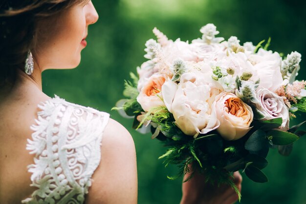 Foto sposa tenera che tiene un mazzo di nozze. sposa sulla natura con un bouquet di peonie.