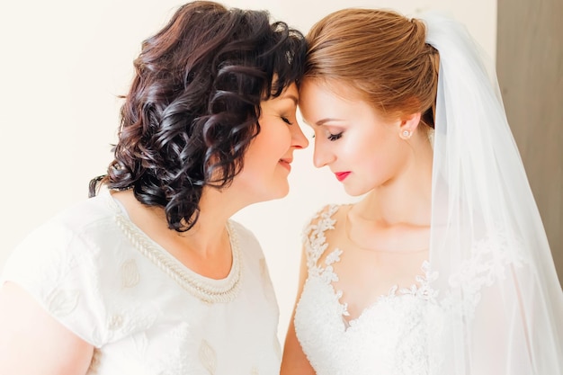 Tender bride and mom hug and touch their foreheads on the\
wedding day mother and daughter relationship concept