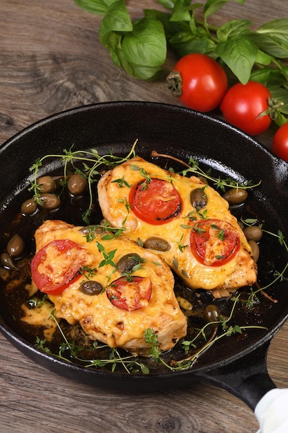 Tender chicken breast baked with tomatoes capers herbs under cheese crust in a frying pan