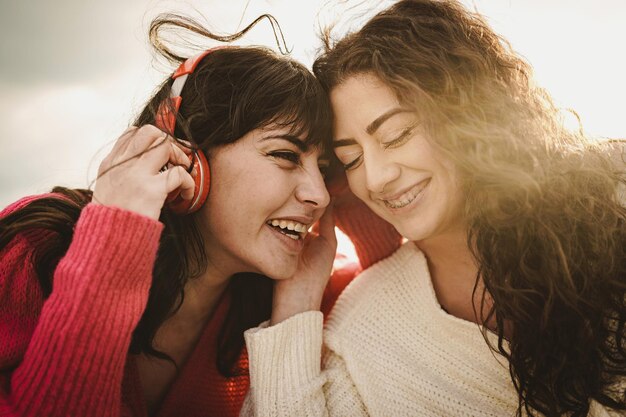 Tender couple of young girlfriends carefree outdoors listening and sharing music from headphones