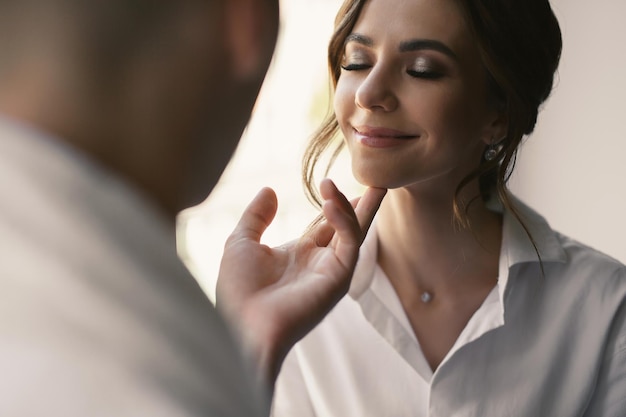 Tender embrace of the bride and groom in white coats in a hotel room