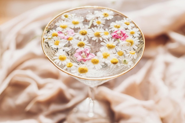 Tender floral aesthetic creative summer image with space for\
text bohemian mood wildflowers in water in stylish wine glass on\
background of soft beige fabric