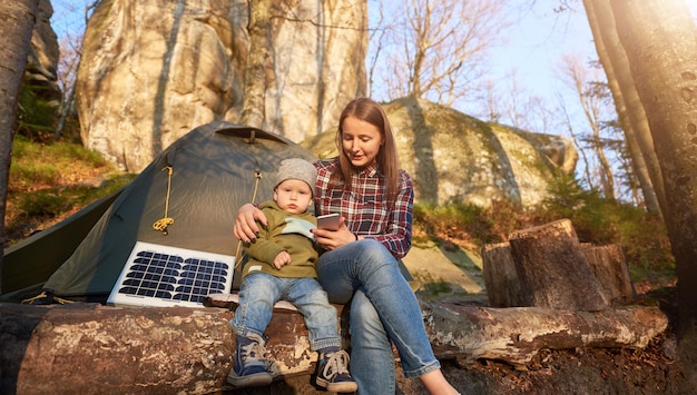 Tender girl and small child are sitting on log near tent and sol