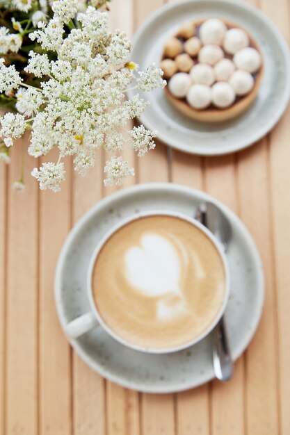 Tender hazelnut tart and cappuccino in white ceramic cup on wooden table at the terrace background Selective focus Aesthetic breakfast on cold autumn weather Flat lay food