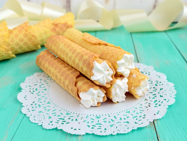 Tender honey wafers in the form of tubes, stuffed with air cream on white lace napkin. Close-up.